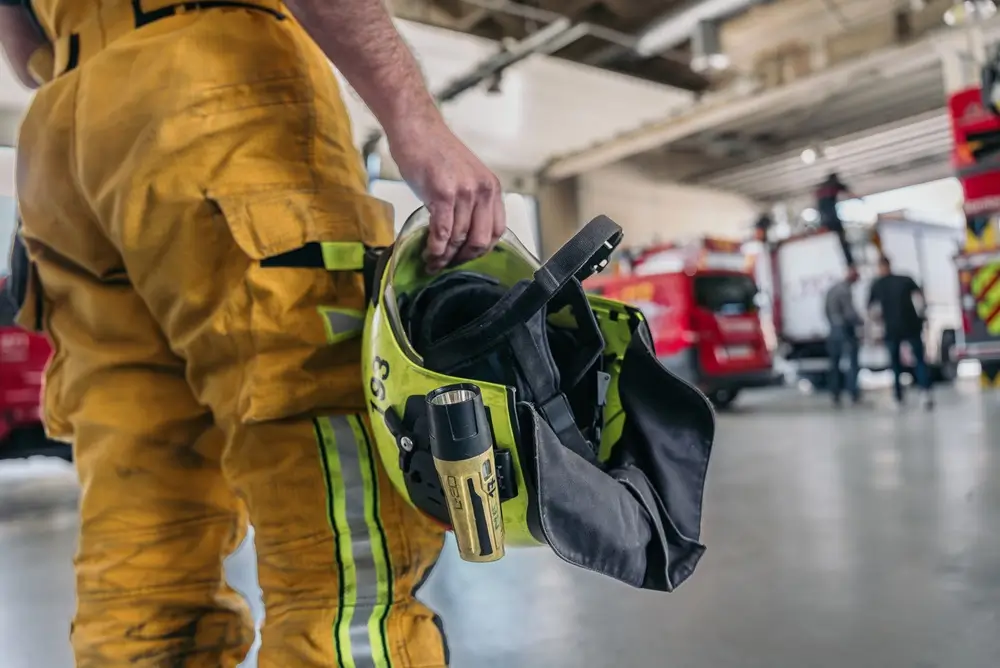 Pompier en tenue dans une caserne de pompiers avec des camions d'incendie garés en arrière-plan.