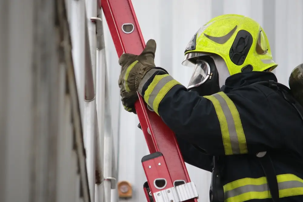 Pompier en formation grimpant une échelle rouge dans un centre d'école du feu lors d'un test de compétences.
