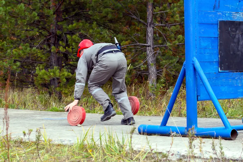 Candidat en plein effort manipulant des tuyaux lors d'un test d'aptitude physique pour devenir sapeur-pompier.
