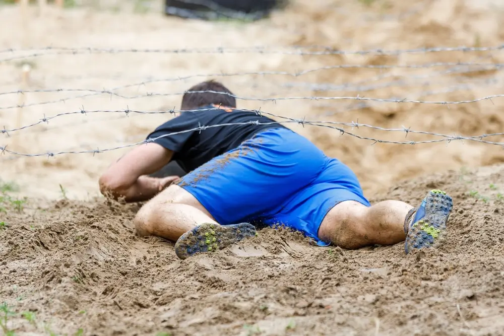 Candidat rampant sous des barbelés lors d'une épreuve physique pour le test de recrutement de pompier.