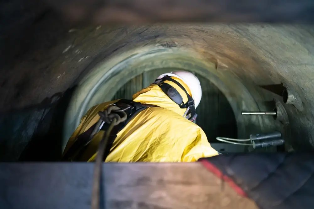Sauveteur en tenue jaune rampant dans un conduit étroit lors d'un exercice d'entraînement en espace confiné.
