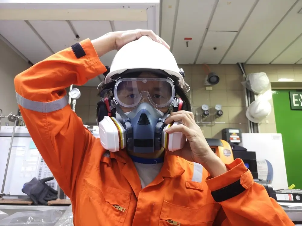 Agent en tenue orange ajustant son masque à filtre respiratoire pour un test de claustrophobie en milieu clos.
