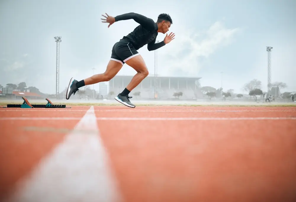 Coureur en plein sprint sur une piste d'athlétisme lors d'un entraînement pour l'épreuve physique éliminatoire.