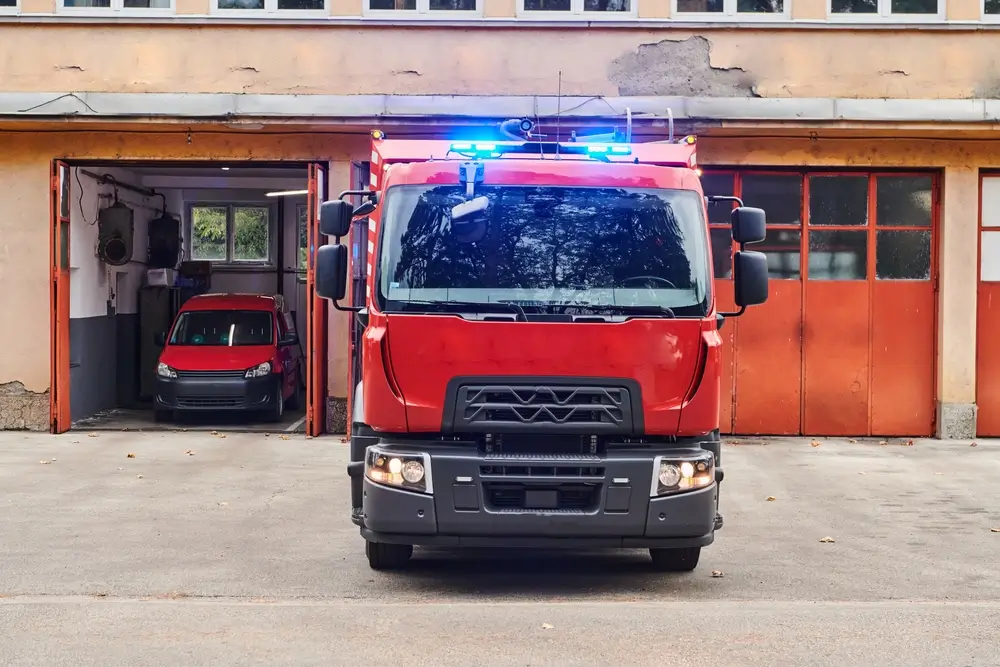 Camion d'intervention rouge avec gyrophares bleus devant les garages d'une caserne de la Protection civile.