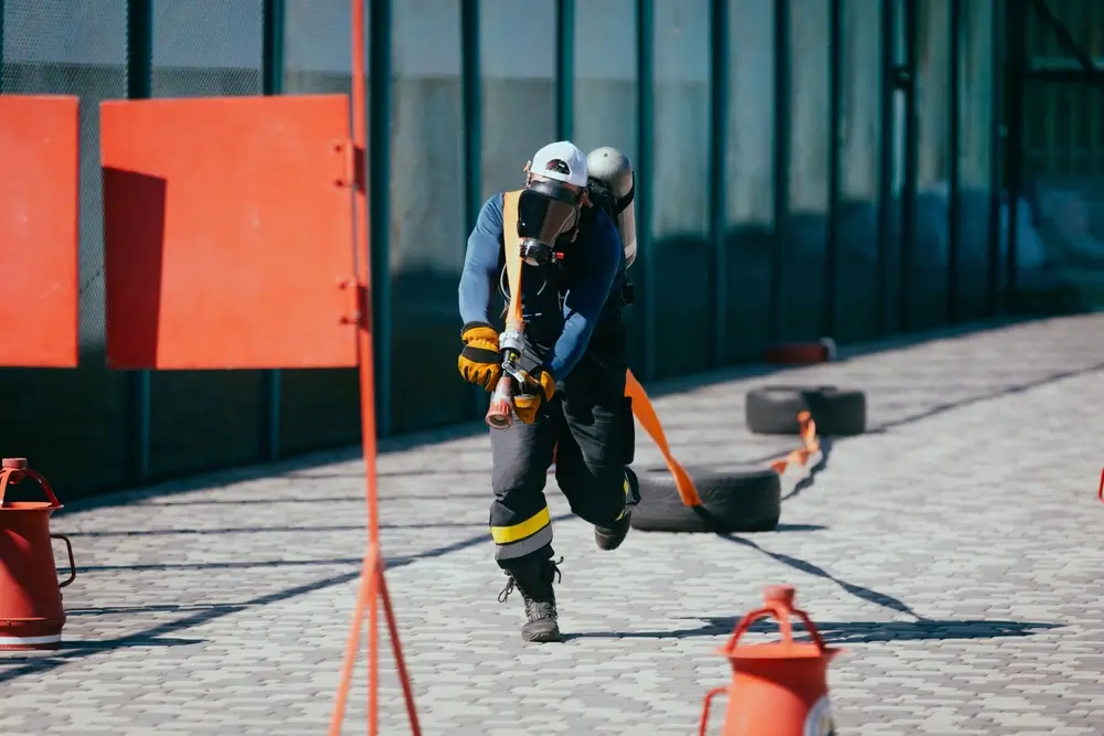 Candidat pompier équipé d'un masque tirant un pneu lors d'une épreuve physique de test d'aptitude en école du feu.