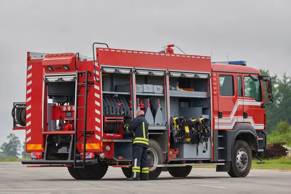 Camion de secours de la Protection civile avec compartiments ouverts et agent préparant le matériel d'intervention.