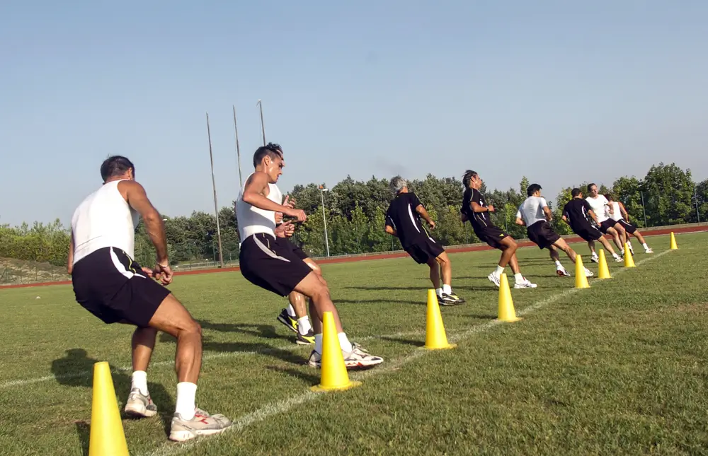 Groupe de candidats réalisant un test physique d'agilité entre des plots sur un terrain d'entraînement sportif.