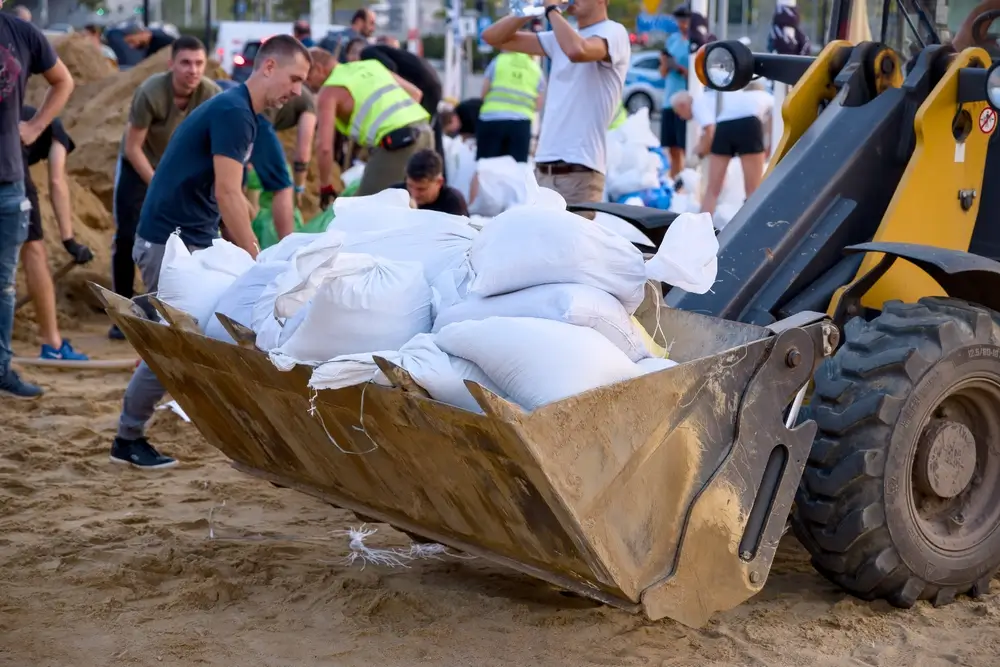 Bénévoles préparant des sacs de sable dans le godet d'une excavatrice pour lutter contre une inondation.