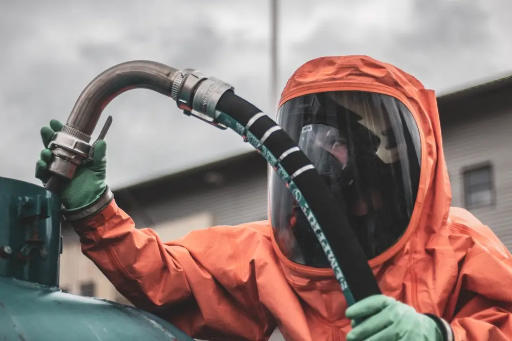 Membre d'une équipe de décontamination NRBC en combinaison manipulant un tuyau lors d'un exercice à Brasschaat.