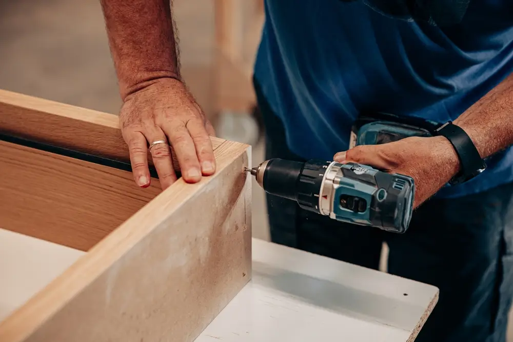Homme utilisant une perceuse sur du bois en atelier lors d'une épreuve technique d'habileté manuelle opérationnelle.