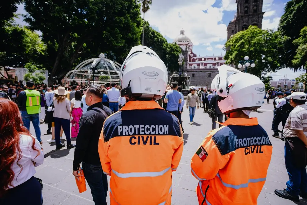 Agents de la protection civile vus de dos, équipés de casques blancs et de vestes de sécurité orange haute visibilité.