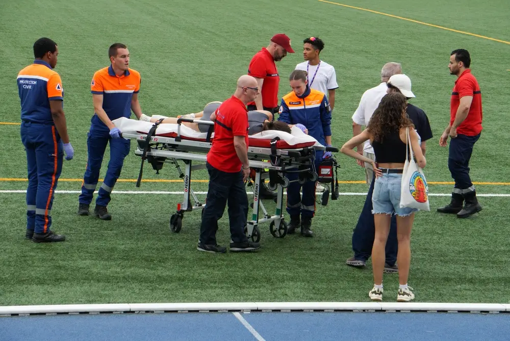 Agents de la protection civile manipulant un brancard lors d'une intervention de secours sur un terrain de sport.